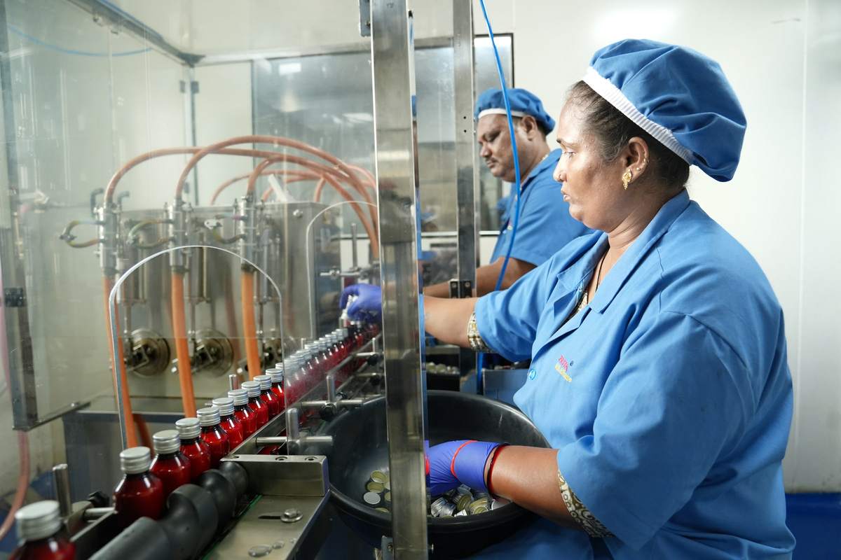 Operator in gloves feeding caps beside an automated liquid filling and capping line with amber bottles